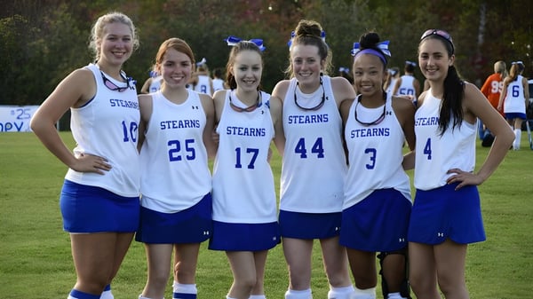Seis estudiantes en uniformes deportivos de la Stearns High School están juntas afuera frente a árboles y áreas verdes.