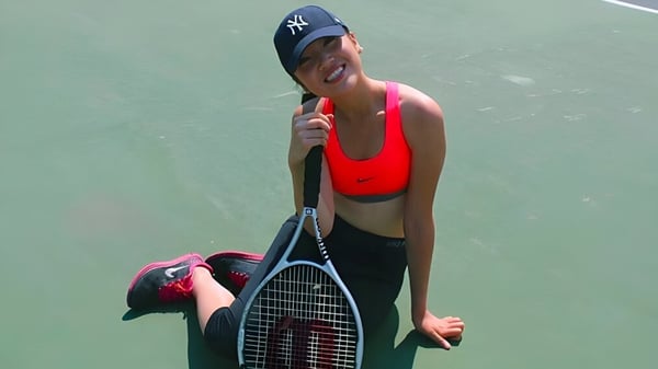 Una persona con una camiseta sin mangas roja y pantalones cortos negros sostiene una raqueta de tenis en el campo de tenis del Stephen Leacock Collegiate Institute.