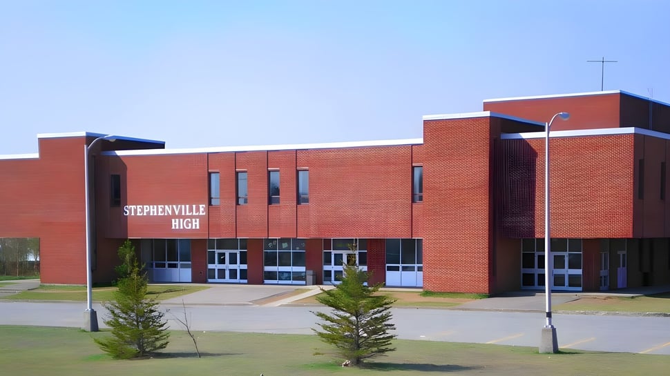 El edificio de ladrillo rojo de la Stephenville High School está rodeado de árboles y se encuentra en una zona pavimentada.