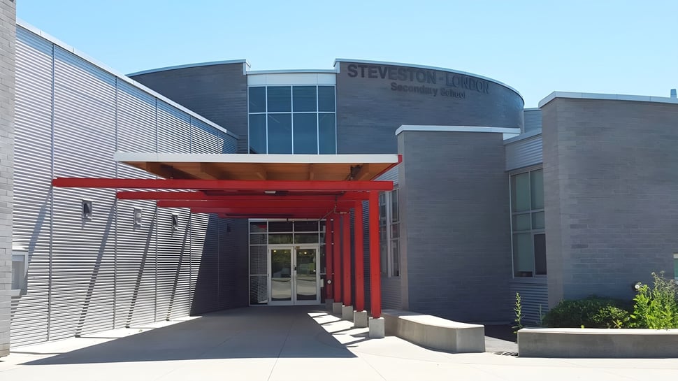 El edificio de varios pisos de la Steveston-London Secondary School muestra una entrada roja con grandes ventanas y un área exterior pavimentada.