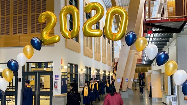 Estudiantes de la Steveston-London Secondary School están de pie en un salón bajo grandes globos dorados de 2020 en sus togas de graduación.