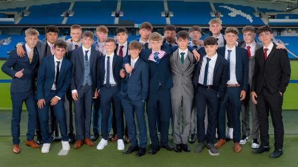Un grupo de jóvenes en ropa formal está de pie en el campo de deportes de Steyning Grammar School and Sixth Form con un gran estadio al fondo.