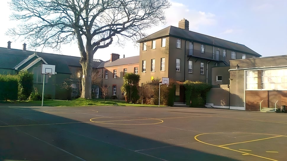 El edificio de ladrillo de varios pisos de la St. Mary’s Secondary School en Baldoyle con una cancha de baloncesto en primer plano y rodeado de árboles.