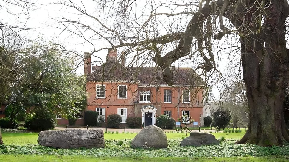Un edificio histórico de ladrillo con entrada de columnas en el terreno del Stoke College rodeado de árboles desnudos y grandes piedras.