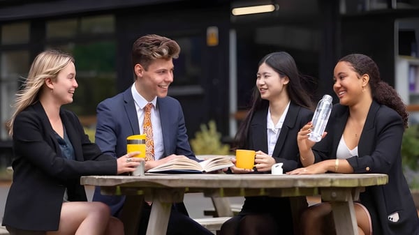 Cuatro jóvenes adultos llevan a cabo una ronda de conversación en la mesa exterior en el campus del Stoke College.