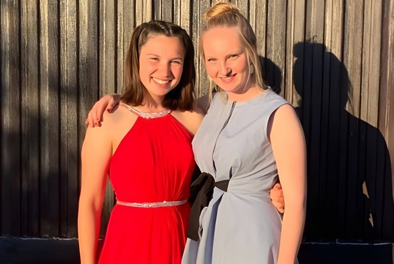 Dos mujeres sonrientes están de pie frente a una valla de madera en el terreno de la Stonar School.