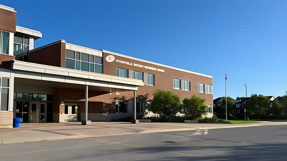 El gran edificio de ladrillo con la entrada principal de la Stouffville District Secondary School está rodeado de árboles y un área pavimentada.