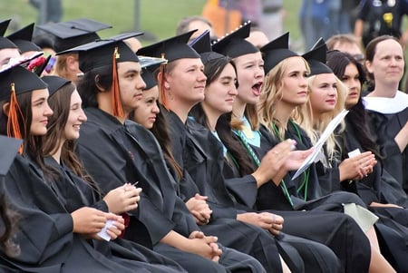 Un grupo de graduados de la Stover School está sentado juntos en togas negras y aplaude durante una ceremonia de graduación.