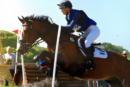 Una estudiante de la Stowe School monta un caballo marrón en un prado verde con una estructura dorada al fondo.