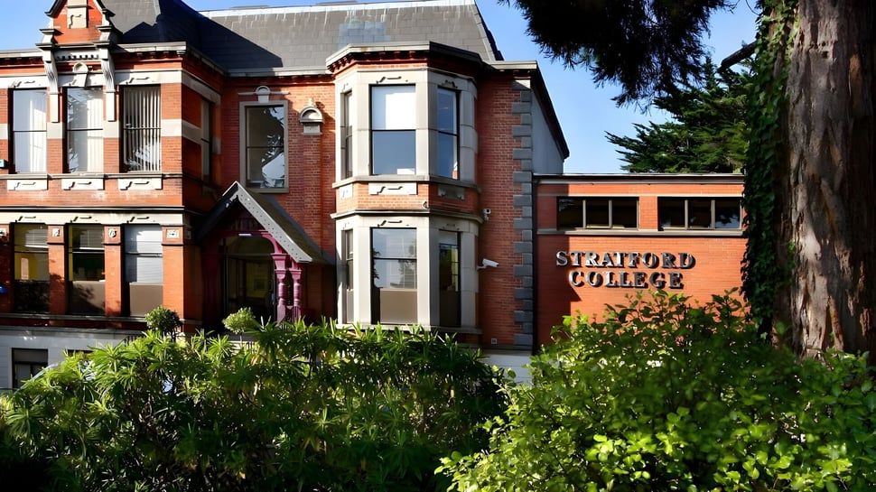 El edificio histórico de ladrillo con detalles arquitectónicos decorativos en el campus del Stratford College está rodeado de vegetación verde.