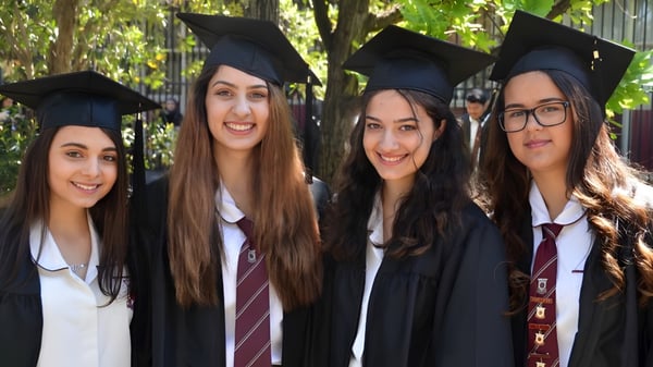 Cuatro estudiantes en trajes de graduación posan sonriendo en el bosque en el terreno del Stretton State College.