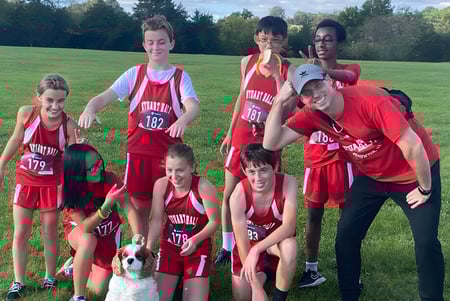 Un grupo de jóvenes atletas en camisetas rojas posan en el campo al aire libre en el terreno de la Stuart Hall School.