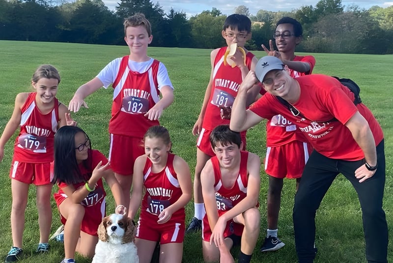 Un grupo de jóvenes atletas en camisetas rojas posan en el campo al aire libre en el terreno de la Stuart Hall School.