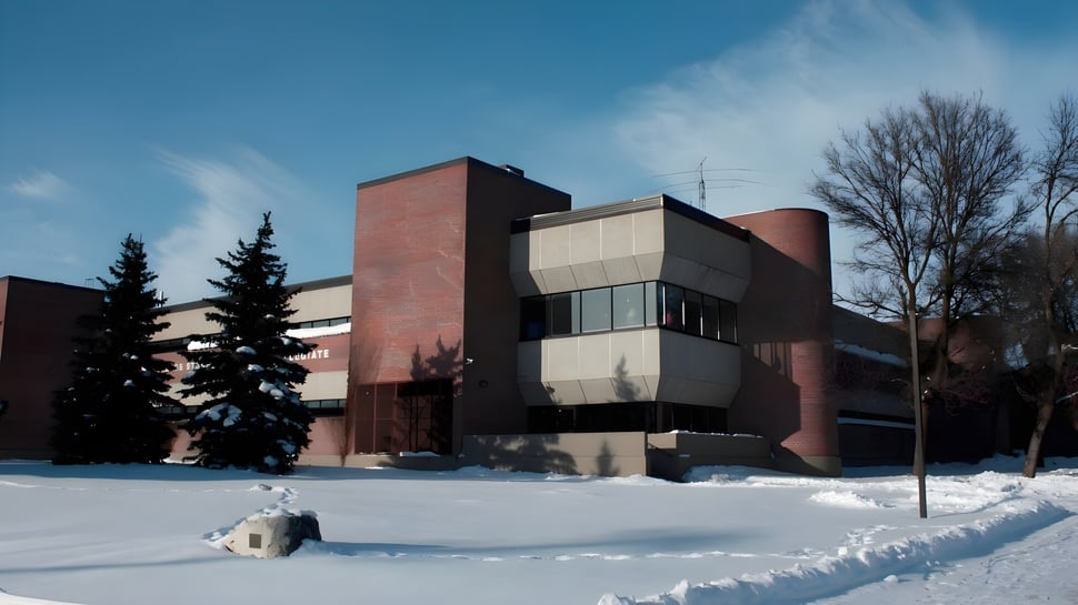 El moderno edificio del Collège Sturgeon Heights Collegiate se encuentra en un paisaje nevado con pinos y cielo azul.