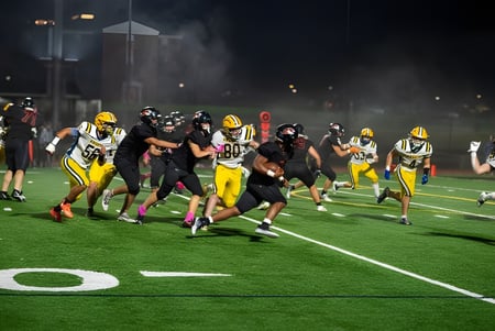 Estudiantes de la Suffield Academy juegan un partido de fútbol americano en el campo iluminado al atardecer.