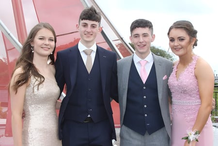 Cuatro personas vestidas de manera formal están juntas frente a un edificio rojo en el campus del Summerhill College.