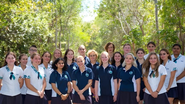 Un grupo de estudiantes en uniformes escolares se encuentra juntos en un bosque verde en el campus de la Sunshine Beach State High School.