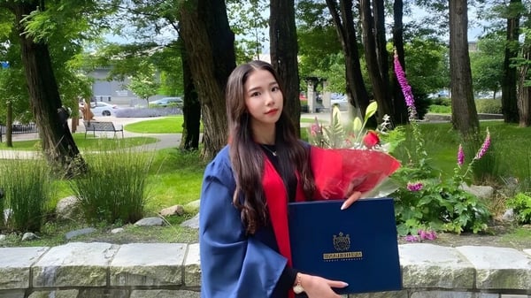 Una estudiante de la Sutherland Secondary School está en el bosque sosteniendo un ramo de flores y un diploma azul.