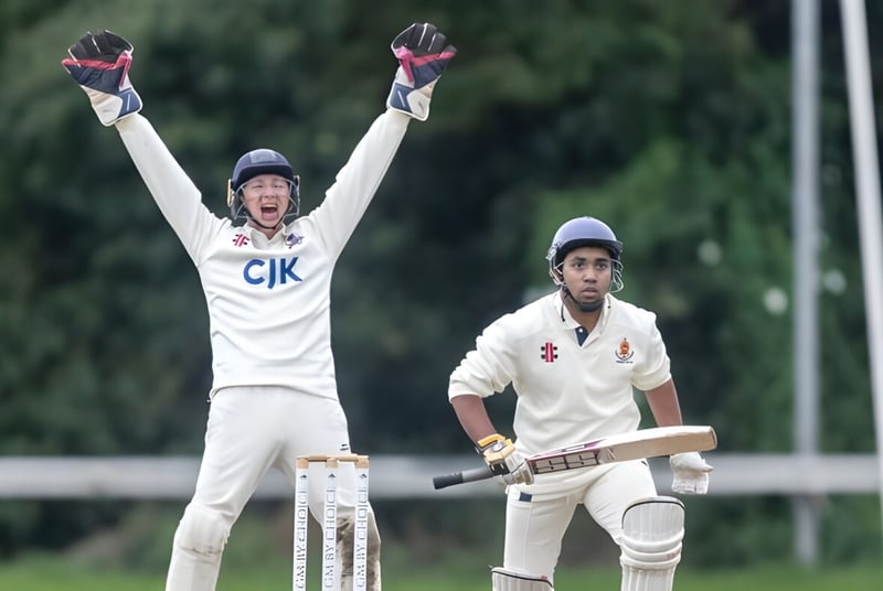 Dos jugadores de cricket en el campo de la Sutton Park School, uno celebra con los brazos en alto, el otro sostiene un bate.