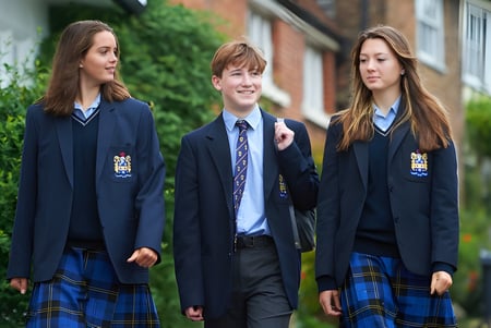 Tres estudiantes de la Sutton Valence School caminan juntos por un camino junto a un edificio de ladrillo en un entorno verde.