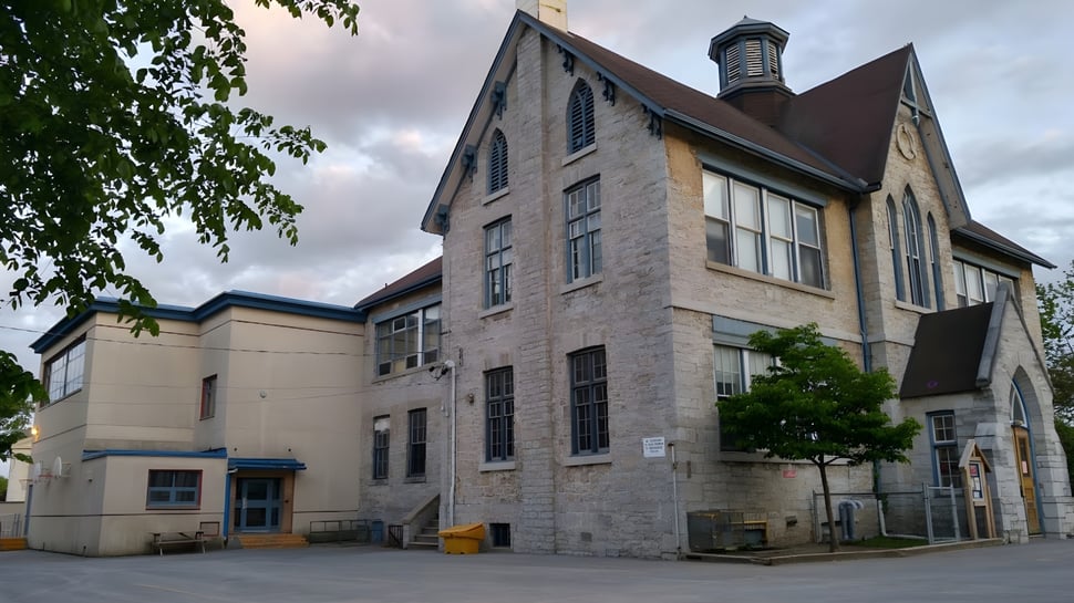 El edificio de ladrillo de varios pisos con una torre distintiva pertenece a Sydenham High School y está rodeado de árboles.