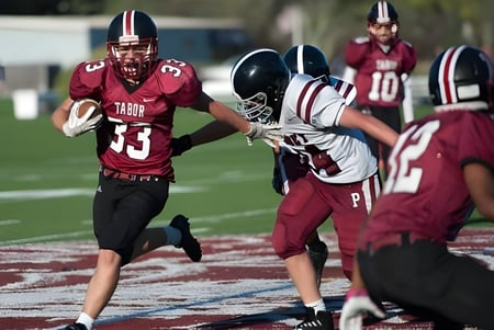 Estudiantes de Tabor Academy juegan un partido de fútbol americano en el campo con ropa deportiva roja y blanca.