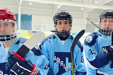 Tres hockeyjugadores en uniformes azules están en el gimnasio sobre la pista de hielo de la Tagwi Secondary School.