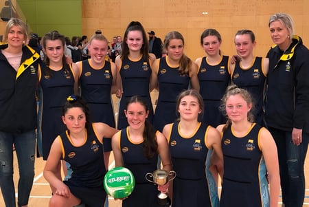 Un grupo de jóvenes atletas del Taieri College sostiene un trofeo en el gimnasio.