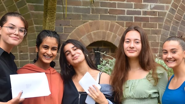Un grupo de alumnas sonríe frente a un edificio de ladrillo con una entrada arqueada en el campus de la Talbot Heath School.