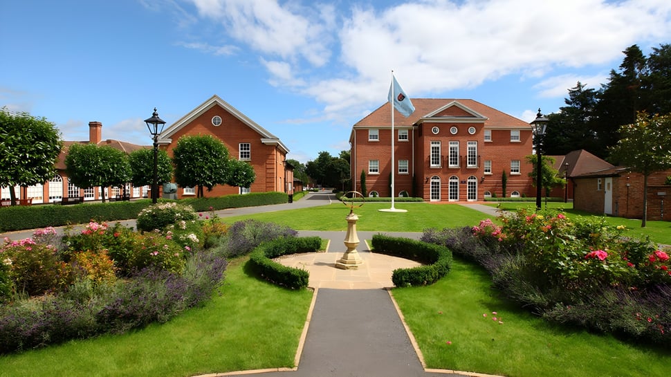 El cuidado jardín con fuente conduce a un edificio de ladrillo con torre del reloj en el campus de TASIS The American International School in England.