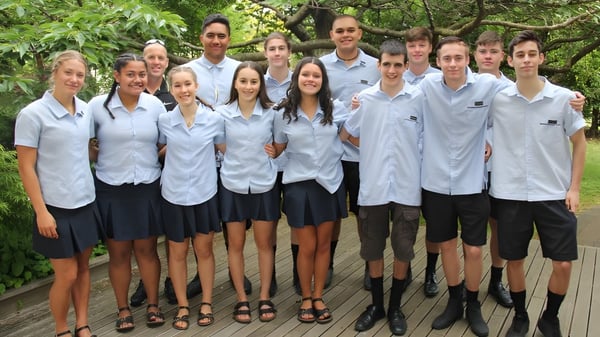 Un grupo de estudiantes en uniformes escolares está junto en el área verde del Tauhara College.