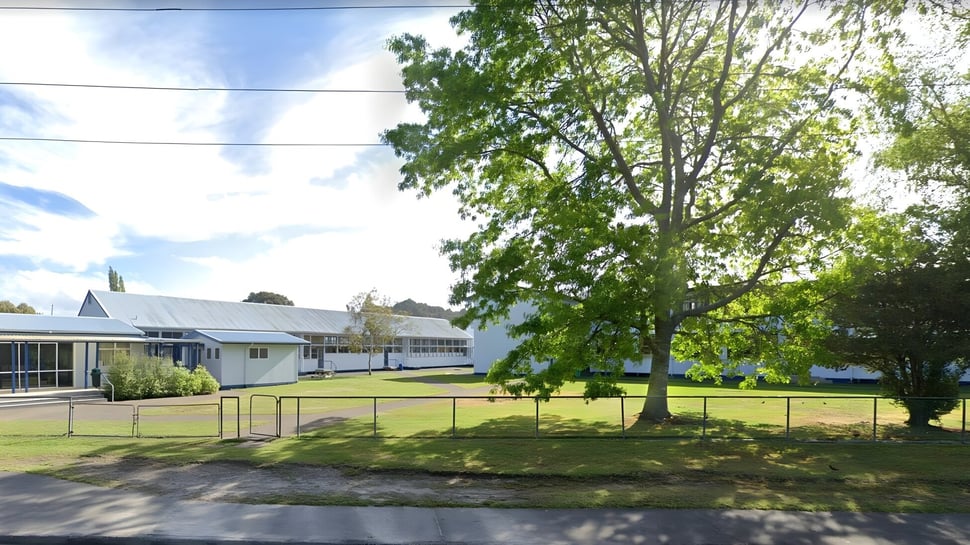 Un campo de césped con árboles y edificios al fondo en el terreno de la Taumarunui High School.