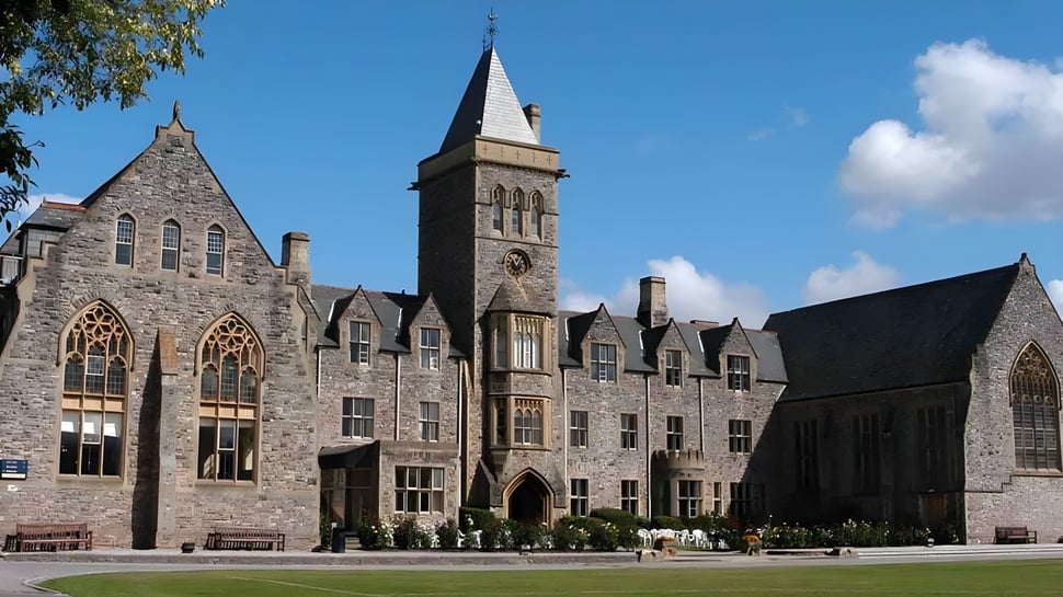 El edificio de piedra medieval de Taunton School International está rodeado de un entorno verde y muestra a personas en primer plano.
