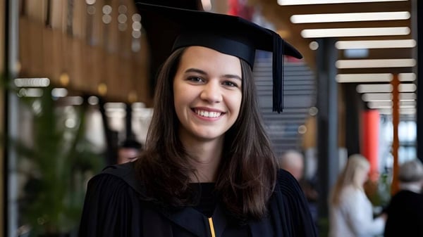 Una graduada sonriente en toga negra está frente a una estructura de madera decorada en el campus de Tauranga Girl´s College.