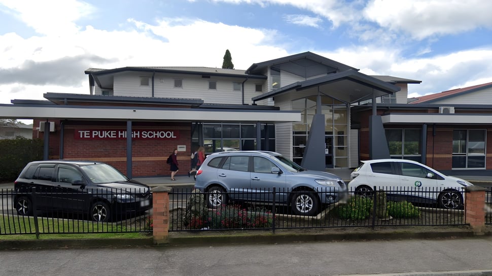 El moderno edificio escolar de la Te Puke High School con un cartel está rodeado de coches estacionados.