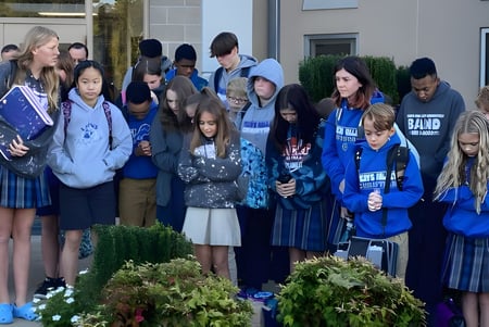 Un grupo de estudiantes de la Teays Valley Christian School está afuera frente a un edificio escolar con plantas de fondo.