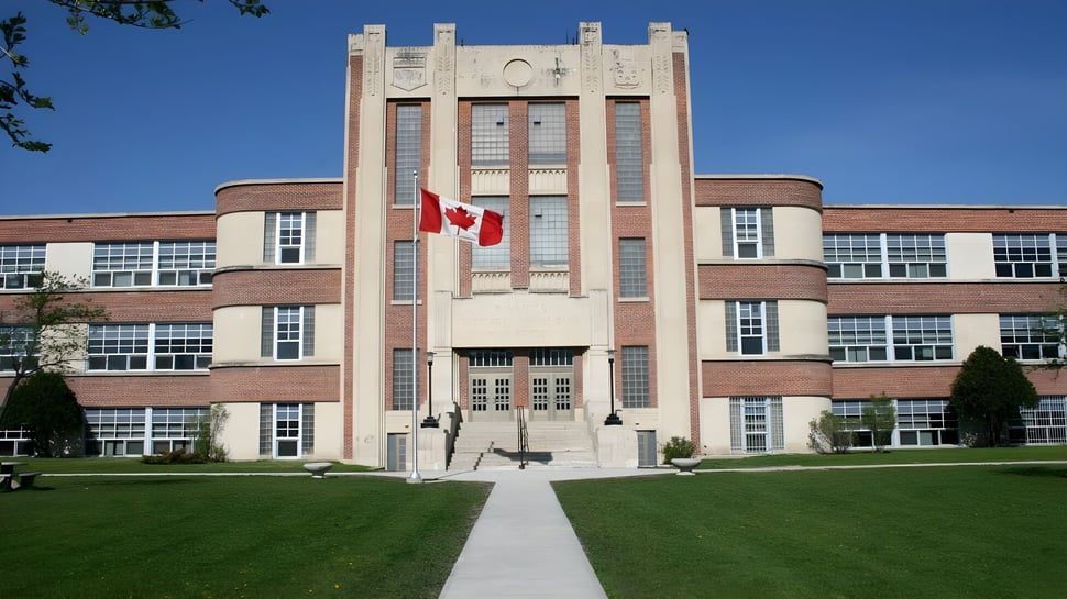 El edificio de la Technical Vocational High School con una torre central y una bandera canadiense está rodeado de un césped cuidado y árboles.