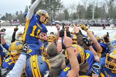 Estudiantes de la Technical Vocational High School celebran juntos en un campo de fútbol nevado con espectadores al fondo.