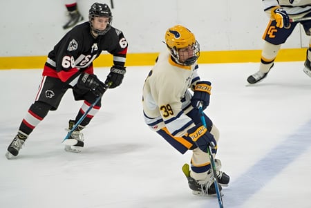 Dos jugadores de hockey con diferentes camisetas juegan sobre el hielo de la Tecumseh Vista Academy.
