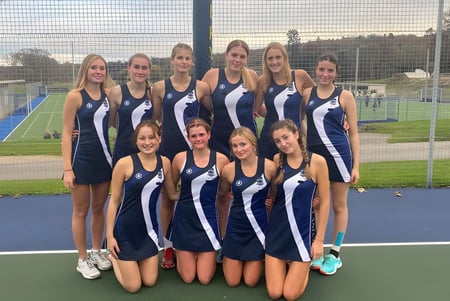 Un grupo de jóvenes deportistas está de pie juntos en el campo de deportes del Templemichael College con una cerca y árboles al fondo.