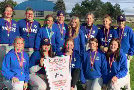 Un grupo de alumnas de la Templeton Academy está en uniformes azules con medallas y un trofeo frente a un edificio deportivo.