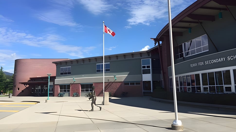 El edificio escolar de varios pisos de la Terry Fox Secondary School con una bandera canadiense y personas en primer plano.