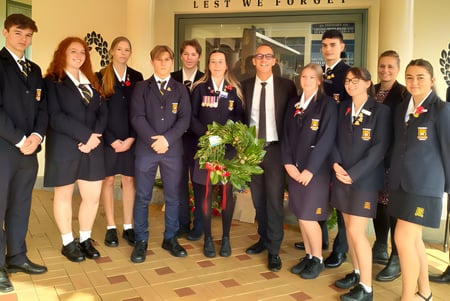 Un grupo de estudiantes de la Thames High School está junto en un pasillo frente a un cartel con la inscripción 'Lest We Forget'.