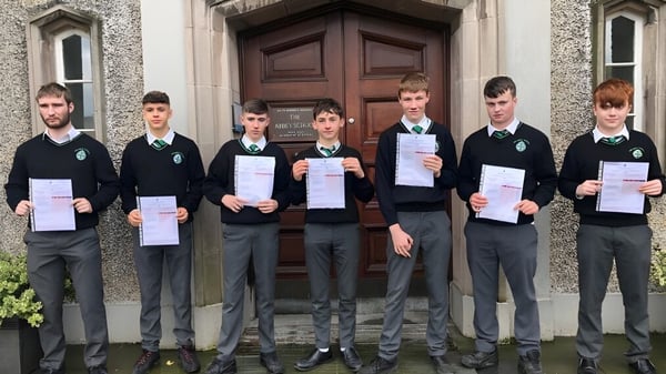 Un grupo de estudiantes de The Abbey School se encuentra frente a una gran puerta de madera y sostiene certificados en alto.