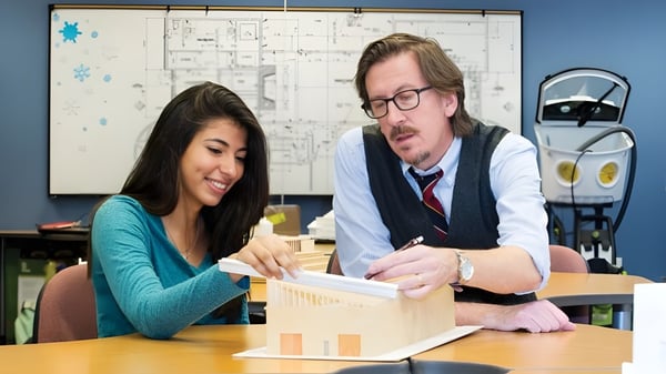 Una joven y un hombre mayor mantienen una conversación en una mesa en un aula de la The Academy MiraCosta.