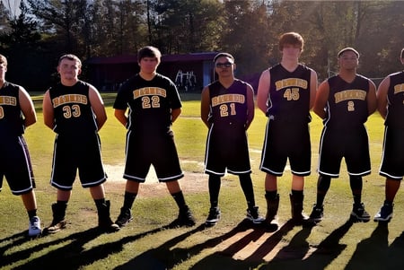 Un grupo de jóvenes atletas está en el campo de deportes de The Barnes Academy frente a árboles y edificios.