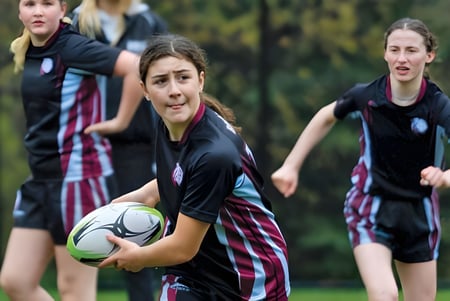 Las alumnas de The Bishop Strachan School juegan al fútbol en un campo de césped con árboles al fondo.