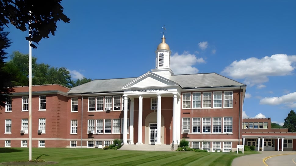 El histórico edificio de ladrillo con un campanario blanco se encuentra en el terreno de The Charles Finney School bajo un cielo azul.
