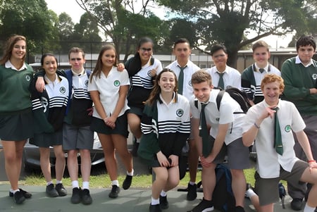 Un grupo de estudiantes de The Forest High School está de pie juntos en un campo con árboles de fondo.