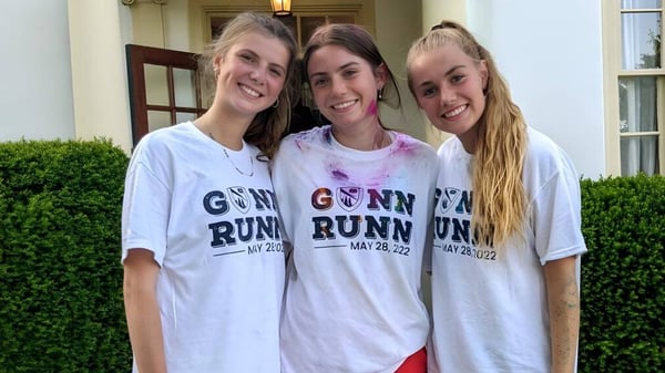 Tres estudiantes de The Frederick Gunn School posan juntas frente a un edificio con un seto verde.
